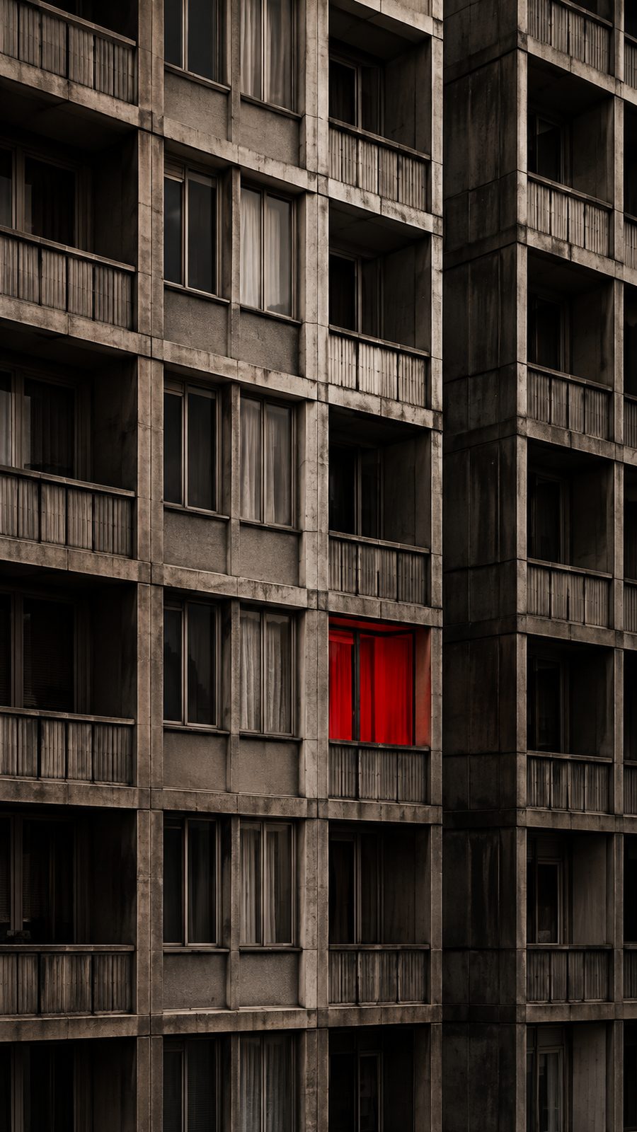 A concrete apartment block with one red window