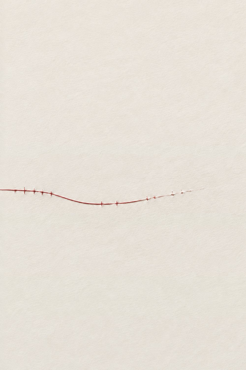 A single red thread drawn across an empty sheet of paper
